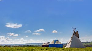 A Hearthworks 18ft diameter Tipi and Yurts of different sizes on a green field with a blue sky