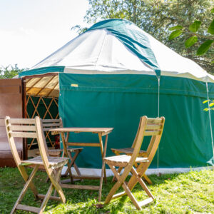 16 ft 5 m diameter Hearthworks Yurt with forest green walls and white roof and wooden door with wooden table and chairs outside