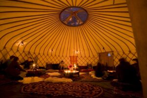 Interior of a 24ft diameter Hearthworks Yurt at night with people relaxing decorative lanterns and sumptuous furnishings