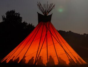 Hearthworks 30 ft diameter Sunlodge Tipi exterior at night showing the shadows cast from the central fire of people sitting around the Tepee